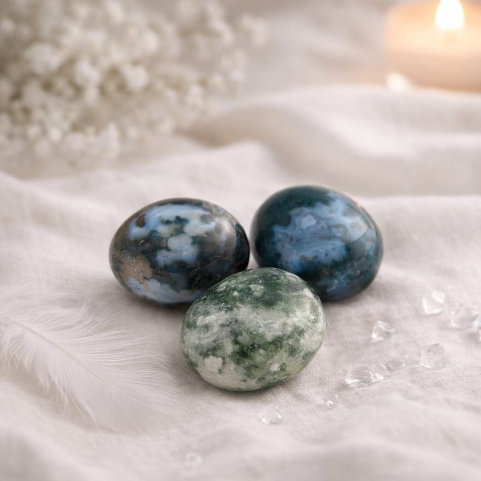 Moosachat Trommelsteine auf hellem Stoffhintergrund mit Teelicht und weißen Blüten.