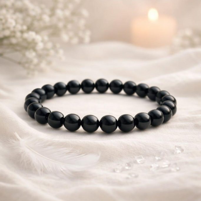 Schwarzes Obsidian Armband auf hellem Stoffhintergrund mit kerze und weißer Blüte als Symbol für die Schutzsteine Übersicht.