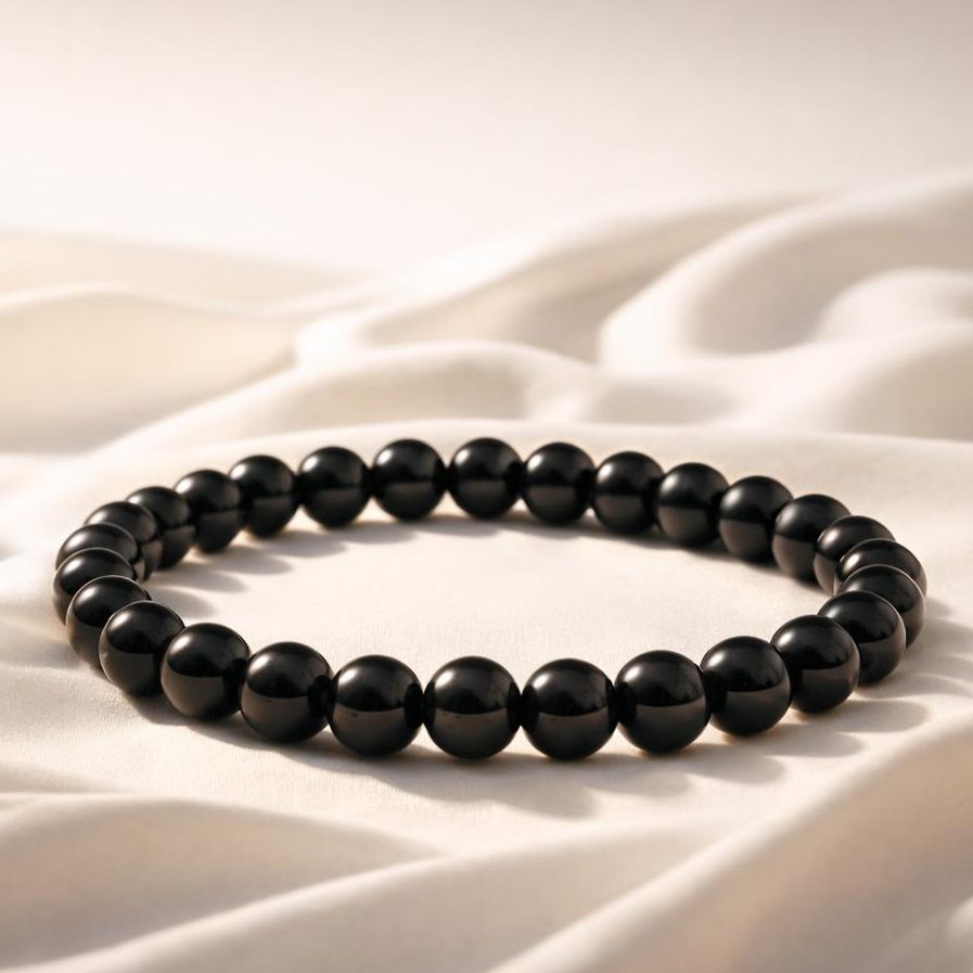 Schwarzes Obsidian Armband auf hellem Stoffhintergund als Symbolbild für das Sternzeichen Skorpion.