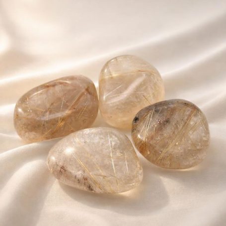 Rutilquarz-Trommelsteine auf hellem Stoffhintergrund – warm goldene Einschlüsse, ruhige Nahaufnahme