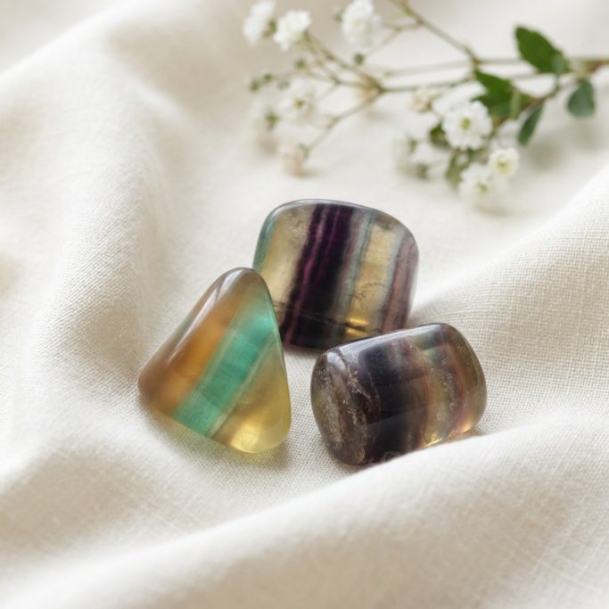 Fluorit Bunt Trommelsteine auf hellem Stoffhintergrund mit weißer Kirschblüte.