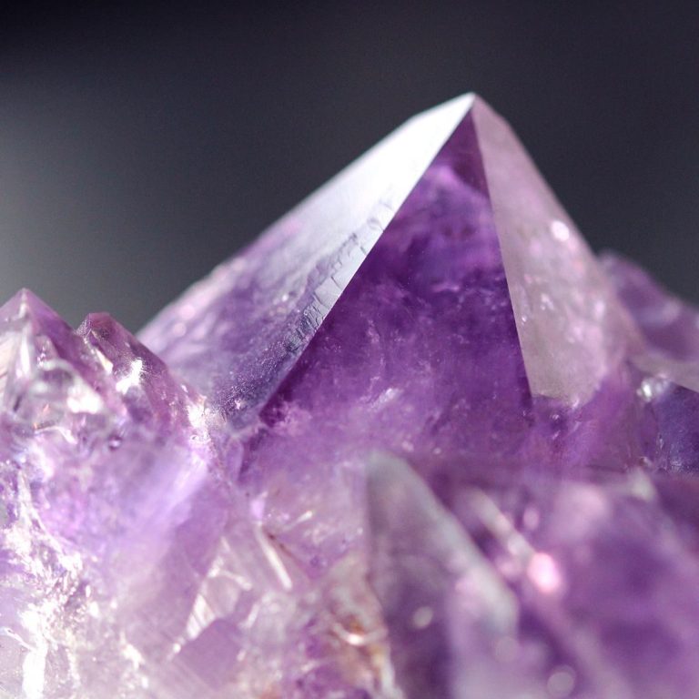 Amethyst-Druse mit violetten Kristallspitzen vor grauem Hintergrund – Symbolbild für die Kategorie Edelstein Lexikon Amethyst