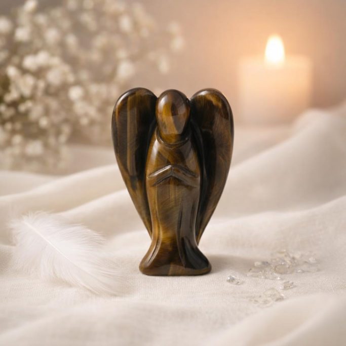 Ein Engel aus Tigerauge auf hellem Stoffhintergrund mit kerze und weißer Blüte als Symbol für die Schutzsteine Übersicht.