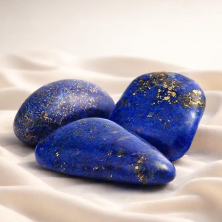 Lapislazuli-Trommelsteine in tiefem Blau mit goldfarbenen Einschlüssen auf hellem Stoffhintergrund
