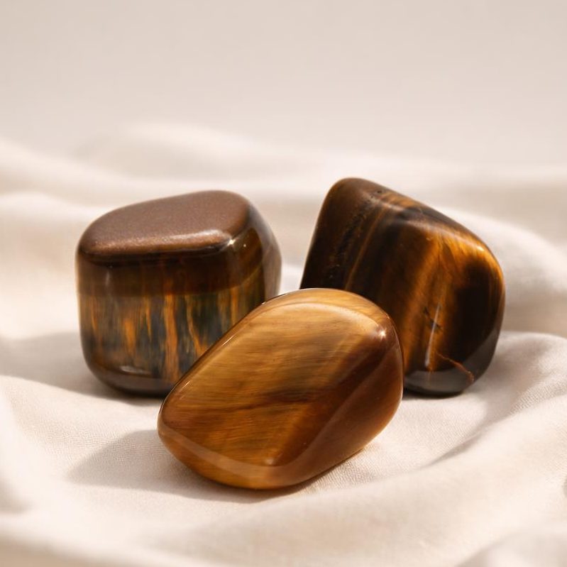 Tigerauge Trommelsteine auf hellem Stoffhintergrund als Edelstein-Klassiker.