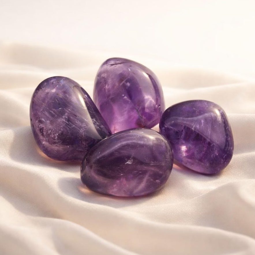 Amethyst Trommelsteine auf hellem Stoffhintergrund als Edelstein-Klassiker.