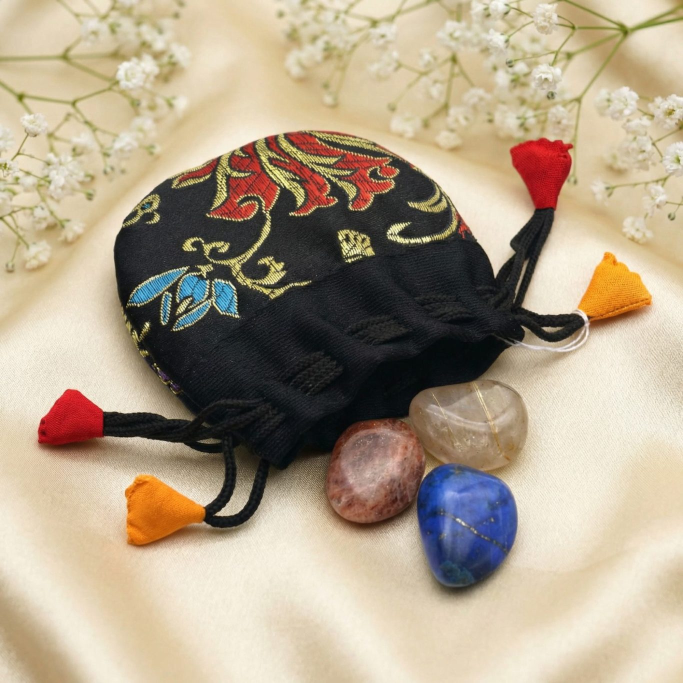 Trommelstein-Set mit Lapislazuli, Rutilquarz und Sonnenstein auf hellem Stoffhintergrund zum Jahr des Feuerpferdes.