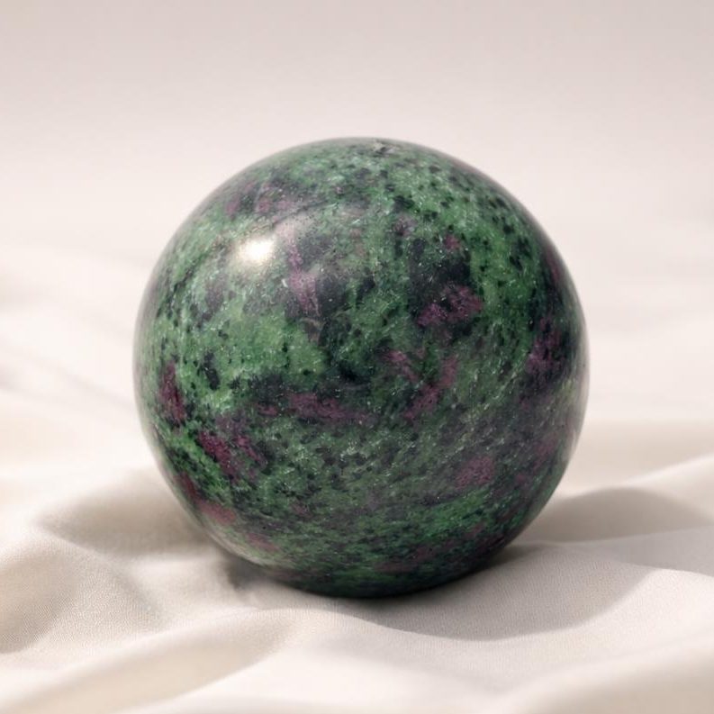 Rubin in Zoisit Kugel auf hellem Stoffhintergrund als Symbolbild für das Sternzeichen Skorpion und seine Edelsteine.