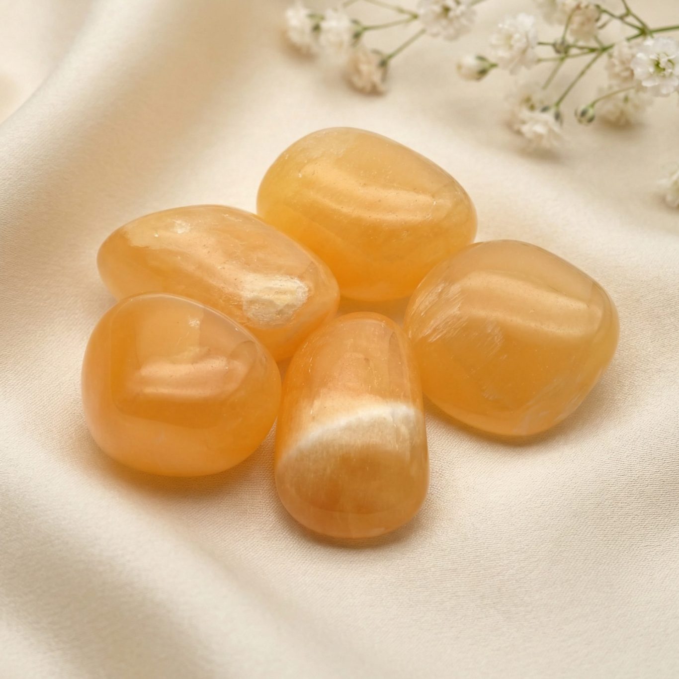 Orangencalcit Trommelsteine auf hellem Stoffhintergrund als symbolische Begleiter für das Sakralchakra.