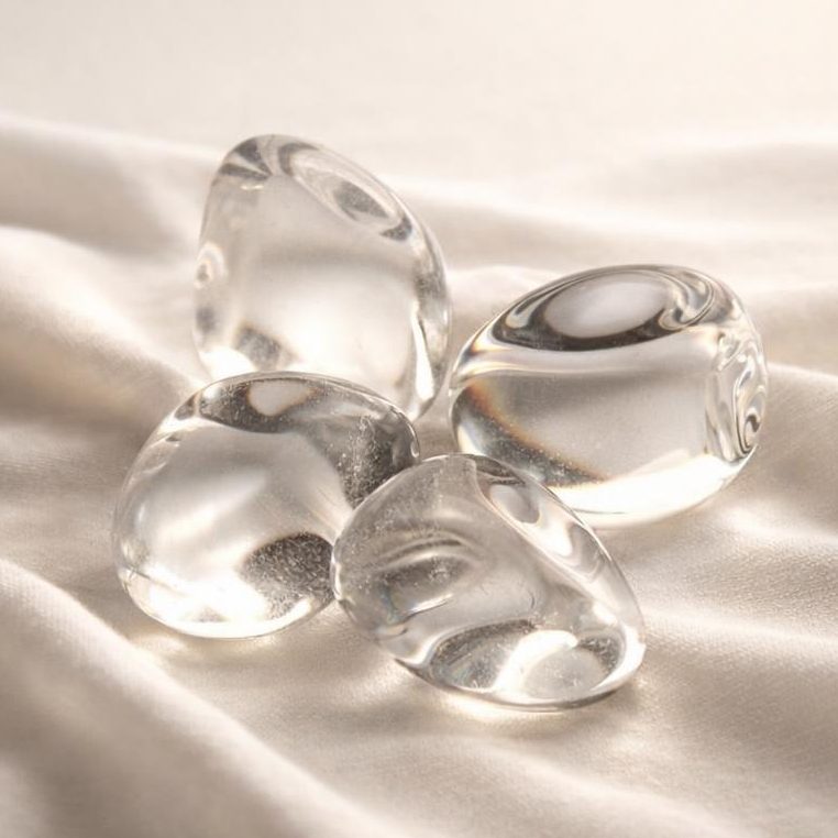 Klare Bergkristall Trommelsteine auf hellem Stoffhintergrund als Symbolbild.