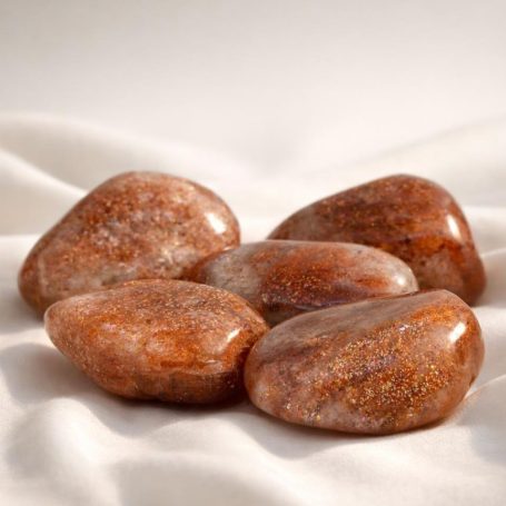 Sonnenstein-Trommelsteine in warmem Orange auf hellem Stoffhintergrund – sanfte, ruhige Produktaufnahme